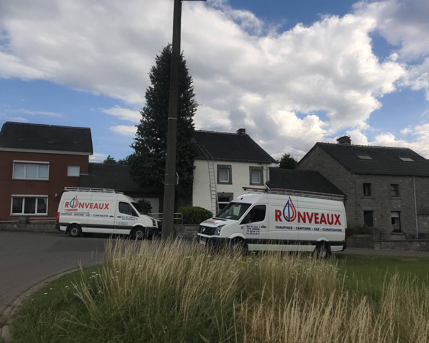 Une vue large d'un d'une ruelle et de 3 maisons. Devant celles-ci, on peut y voir deux camionnettes appartenant à Chauffage Ronveaux.
